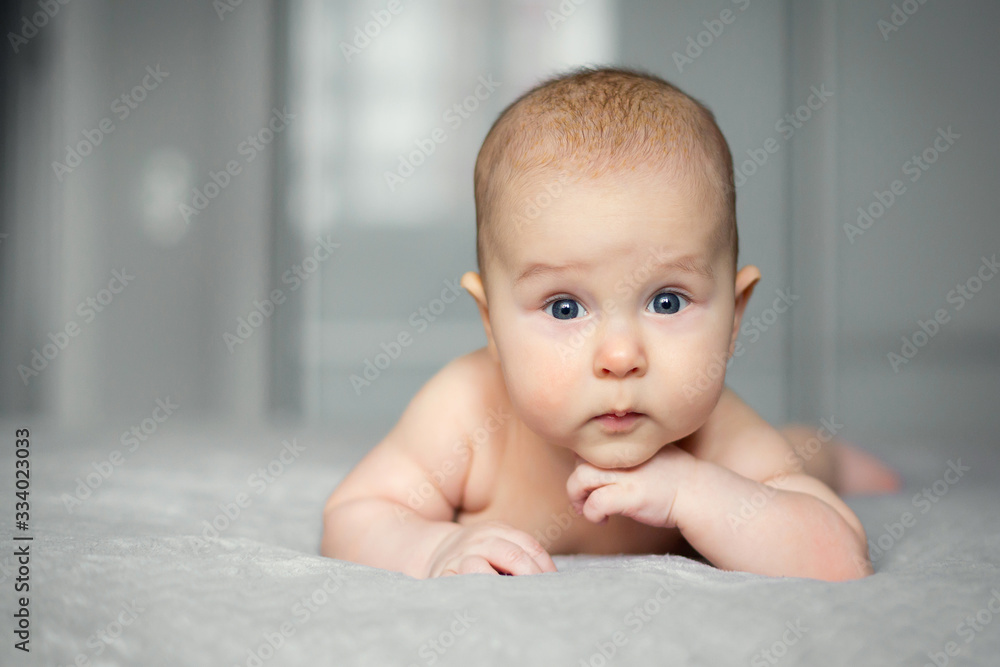 Beautiful smiling baby boy lying on grey blanket and posing