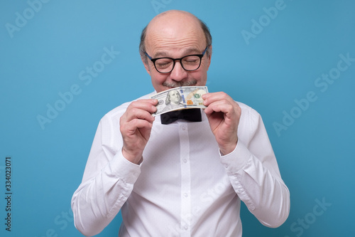 Fotografia Senior caucasian man in glasses hold a dollar banknote and sniff