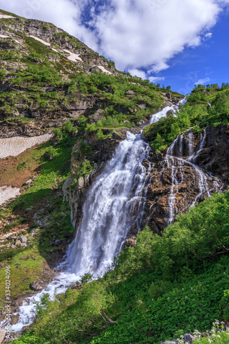 Beautiful scenic landscape of Imeretinskiy waterfall in Caucasus mountains  Karachai-Cherkess Republic. Imeretinka river waterfall at summer in sunlight with splashes and blue sky.