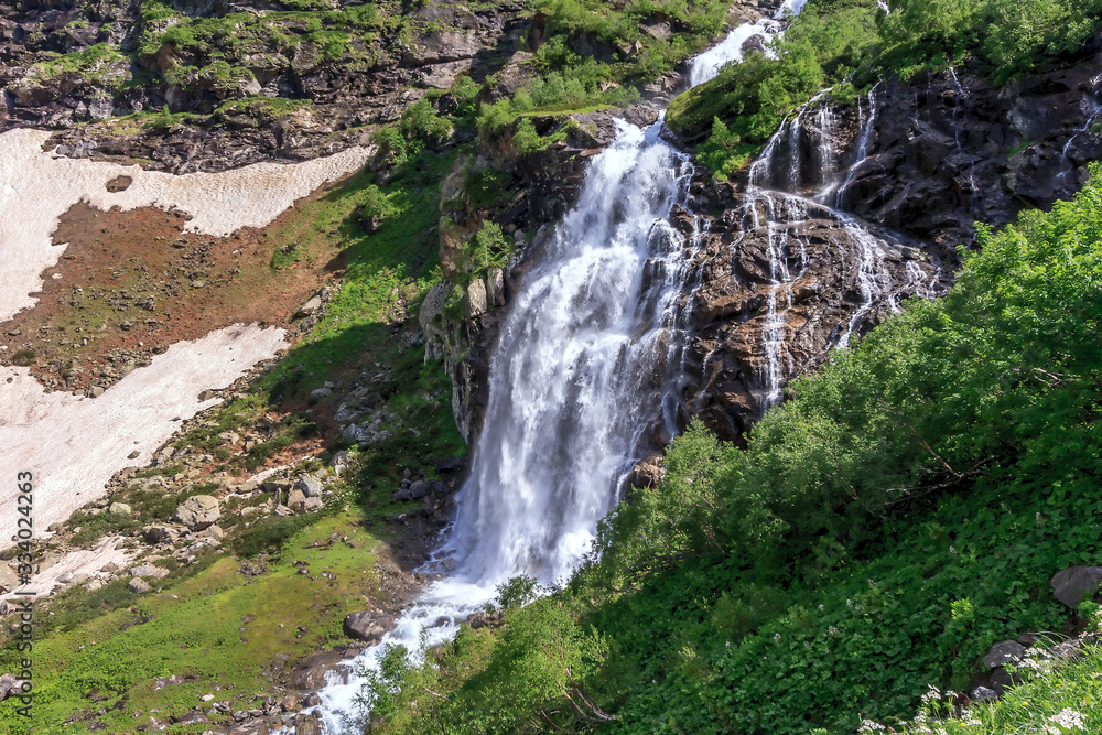 Naklejka premium Beautiful scenic landscape of Imeretinskiy waterfall in Caucasus mountains, Karachai-Cherkess Republic. Imeretinka river waterfall at summer in sunlight with splashes and blue sky.