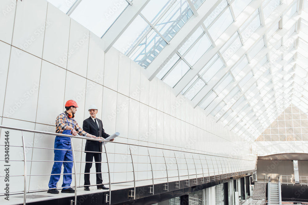 Standing industrial engineers in blue vests and helmets. Glass roof.