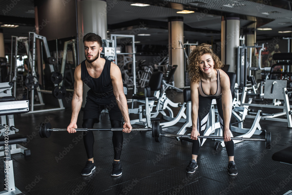 Fitness and young couple exercising in gym with barbell weights