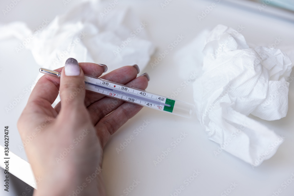 The thermometer in woman’s hand and used napkins around on white table The thermometer in woman’s hand and used napkins around on white table