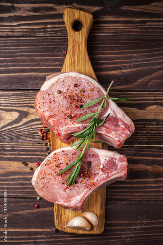 Pork steak with spices and rosemary. Juicy and fresh raw meat with peppercorns on a wooden cutting board on the kitchen worktop. vertical photo
