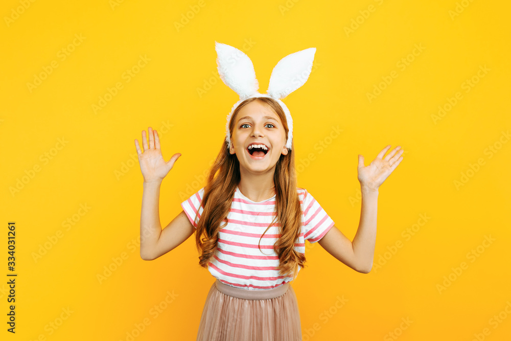 Happy little beautiful girl on her head with rabbit ears, posing on a yellow background