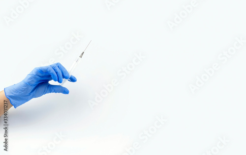 Close-up of a female doctor's hand in a blue sterilized surgical glove with a plastic medical syringe filled with a transparent drug on a white background copy space. Banner, coronavirus. covid-19