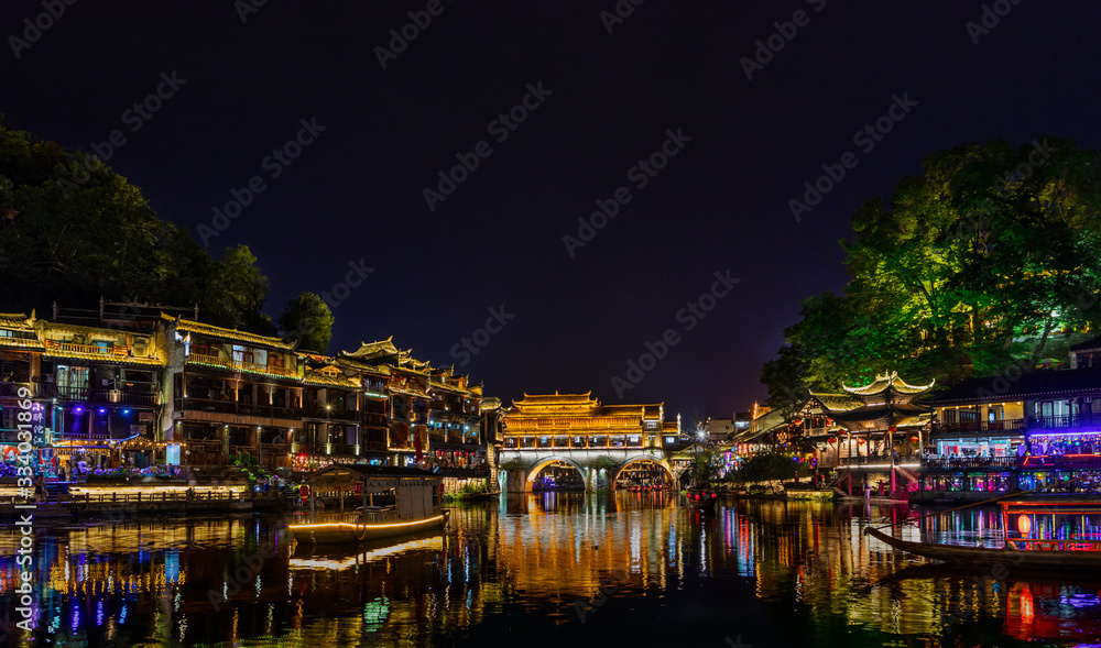 Night view of Hong Bridge & stilt houses of Tujia Minority by riversides of Tuo River in Fenghuang Ancient Town built in 1704 in western Hunan, China. UNESCO World Heritage.