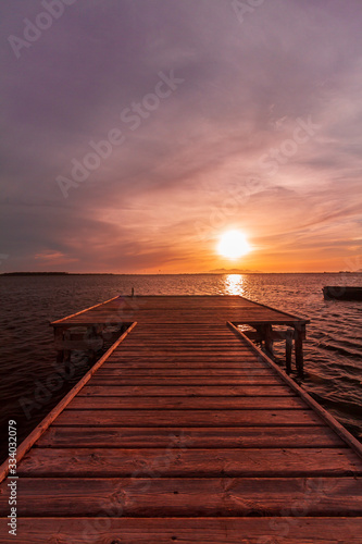 Fototapeta Naklejka Na Ścianę i Meble -  Wooden pier on a warm light during sunset, with violet and orange sky