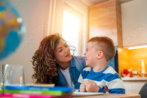Kind mother helping her son doing homework in kitchen. Mother Helping Son With Homework At Table. Children's creativity. Portrait of smiling mother helping son with homework in kitchen at home photo