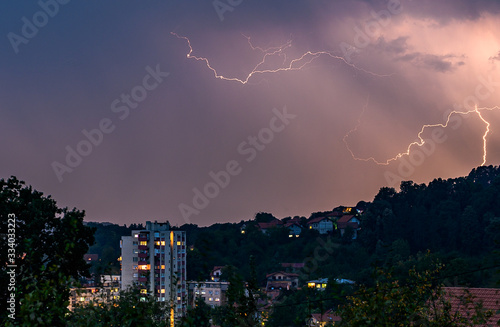 Lightning over the city at the summer storm. Dramatic, breathtaking atmospheric natural phenomenon.Beautiful dark storm sky. Clouds and thunder lightnings.Bright lightning in the black sky