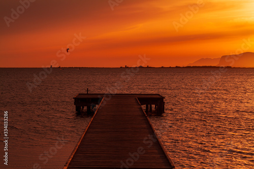 Wooden pier on a warm light during sunset  with orange sky and a Kite surf and two mountains silhouette in the background