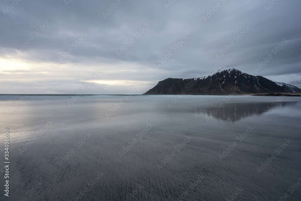 Skagsanden beach in Lofoten, Norway during blue hour and cloudy weather. Long exposure shot to capture silky smooth waves. Fine art and traveling concept.