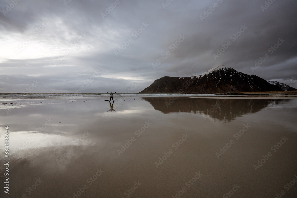 Fotografie Man stands on skagsanden beach during blue hour with arms stretched out
