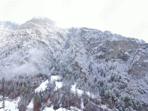 Aerial view of mountain with boundary tower, forest underneath fog, slopes with snow covered in Switzerland, cloudy atmosphere, beautiful conditions © Vladimir Drozdin