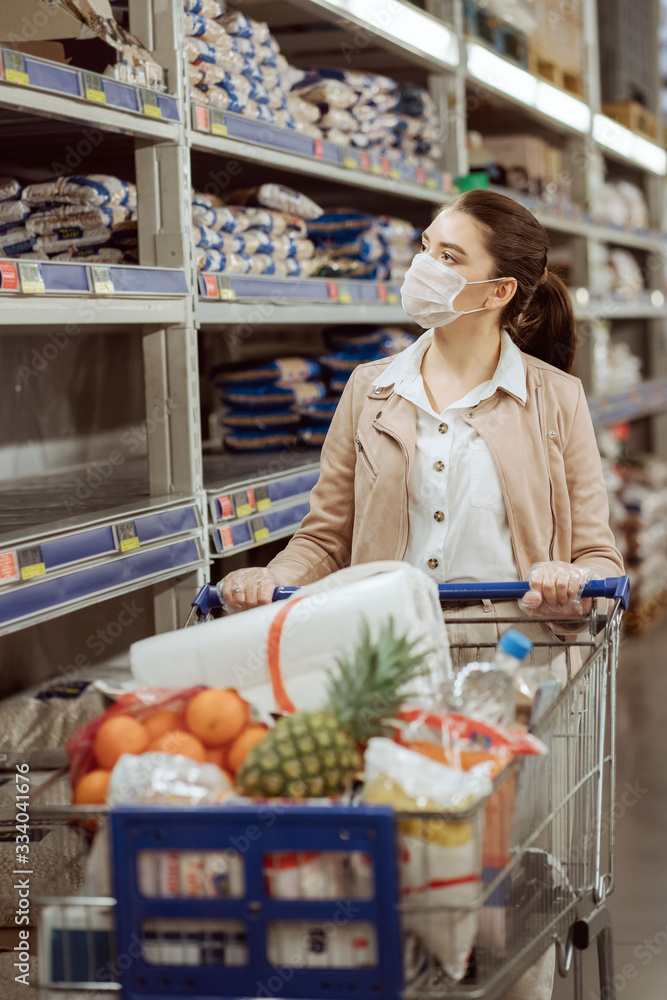 woman with medical facemask looking products in a supermarket. but the shelves are empty and the choice is small.