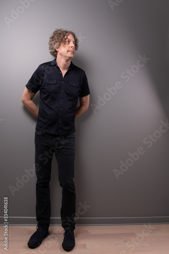 Studio portrait of tall man with cool, vintage style. His hands are behind his back, and he looks up.