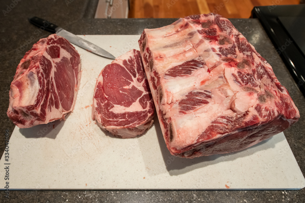 Raw beef prime rib roast and a large cut of meat from a butcher's shop. The grade a beef is being cut into smaller sized roasts. There's marbling and fat throughout the meat on the cutting board. 