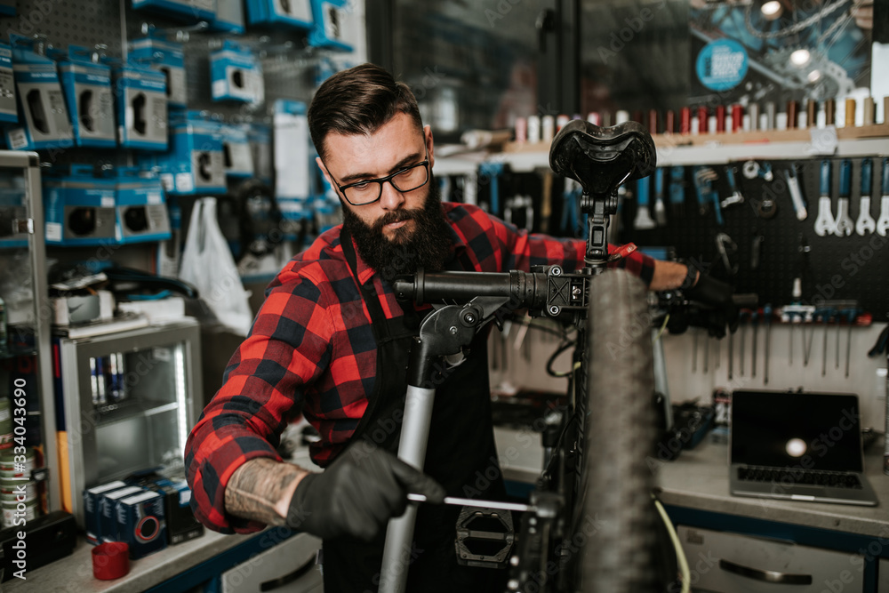 Young beard bicycle mechanic repairing bicycles in a workshop.. Young beard bicycle mechanic repairing bicycles in a workshop..