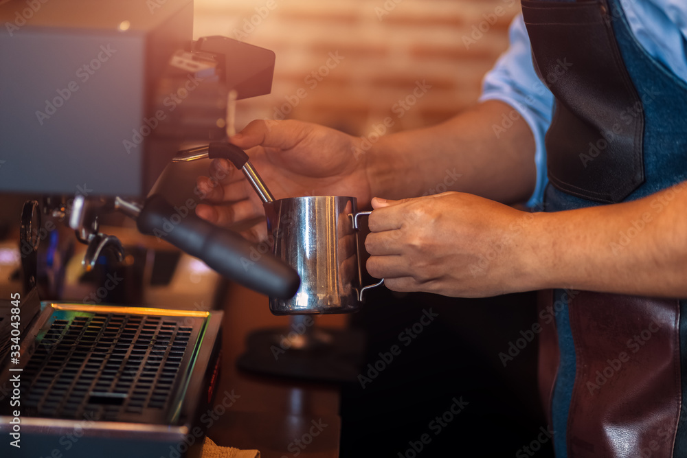 Barista steaming milk in the pitcher with coffee machine for  preparing to make latte art.