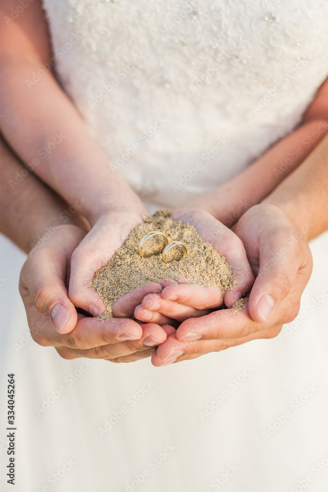 woman hands with sand and wedding rings on beach