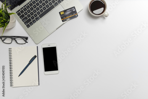 White office desk table with laptop, and smartphone and pen on a notebook, credit card shopping online concept with copy space, top view