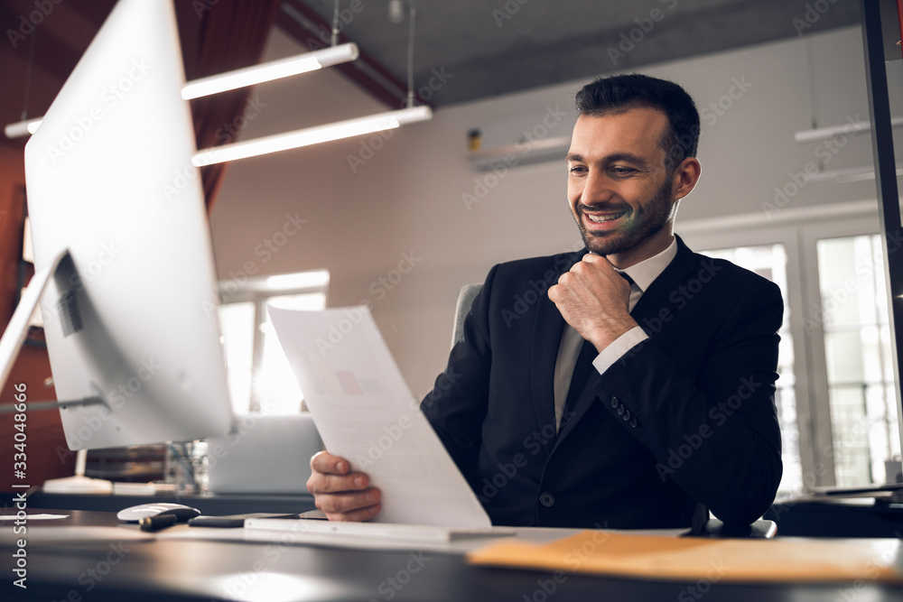Satisfied young boss reading documents in his office Satisfied young boss reading documents in his office