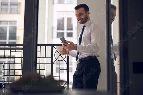 Young happy businessman talking on mobile phone near balcony