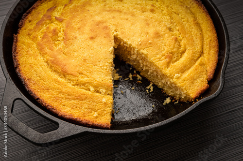 Fresh cornbread right out of the oven baked in a cast iron skillet with a slice removed photo