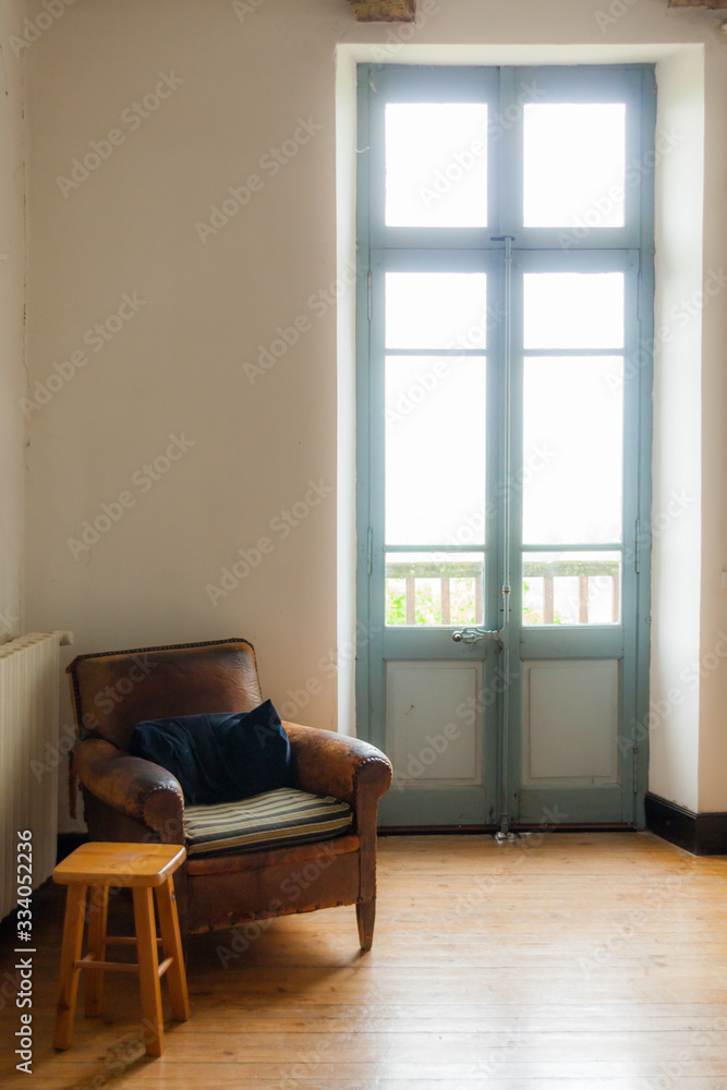 Old leather armchair in corner next to window light from a door Old leather armchair in corner next to window light from a door