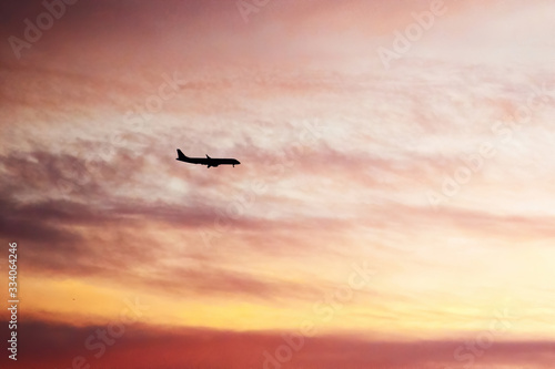 Airplane silhouette in the sunset light high up in the sky with cumulus clouds around. Travel destinations. Twilight sky. Background texture