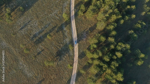 Aerial top down view of car driving on rural road, path near forest. Sunrise in village Grahovo, Montenegro. Countryside. Rural landscape.