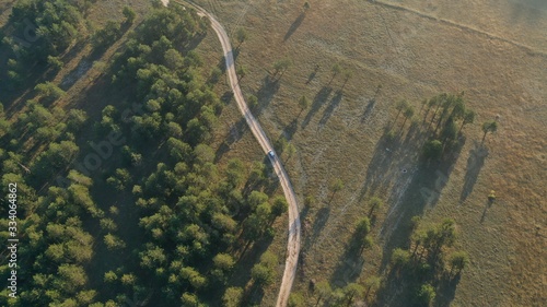 Aerial top down view of car driving on rural road  path near forest. Sunrise in village Grahovo  Montenegro. Countryside. Rural landscape.
