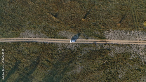 Aerial top down view of car driving on rural road, path in the fireld. Sunrise in village Grahovo, Montenegro. Countryside. Rural landscape. Travel by car, journey. photo