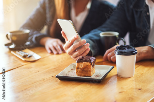 A group of young asian people using and looking at the same mobile phone together in cafe