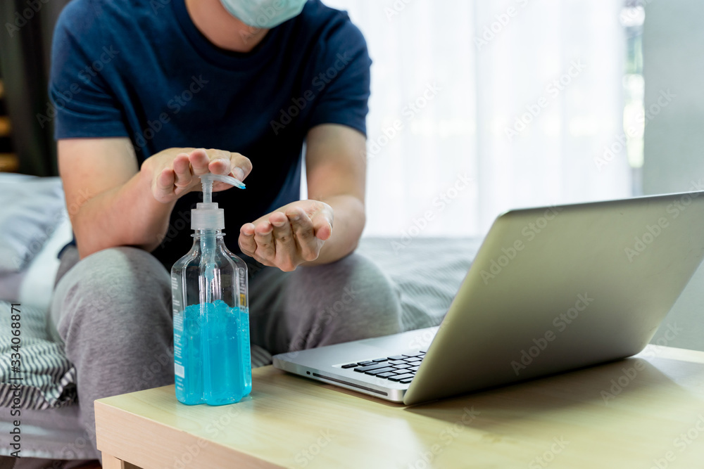 Asian Man working from home wearing protective mask in bedroom. Quarantine for coronavirus wearing protective mask at home. Washing hands with alcohol gel sanitizer to clean hands