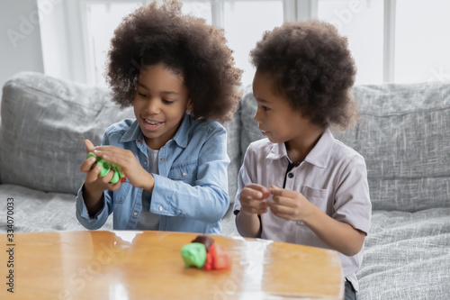 African siblings sit on couch spend time using play dough making diverse shapes have fun together at home  older sister teach younger brother to create. Hobby pastime useful activities for kid concept