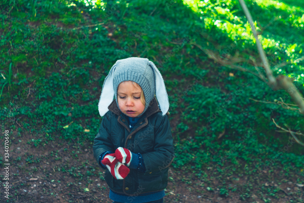 Little preschooler putting on his gloves in the woods Little preschooler putting on his gloves in the woods