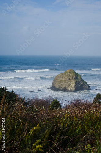 A long view of the large rock cliff formation off the coastline shores of the oregon country side. 