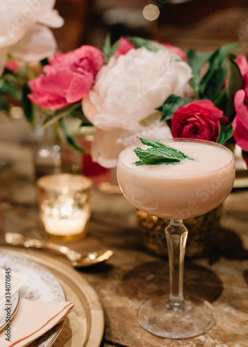 A creamy alcoholic cocktail garnished with mint in a rustic setting with white and pink florals in the background