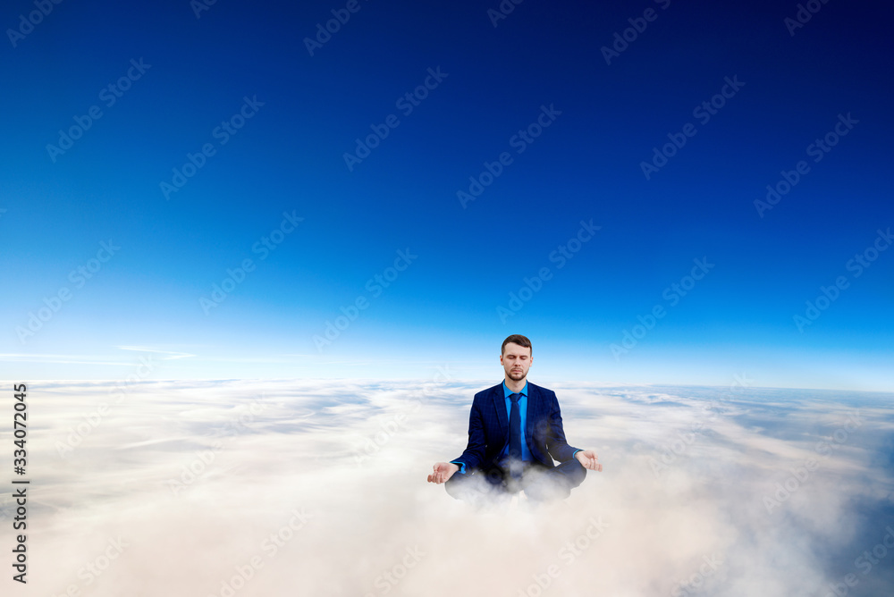 Businessman sitting in lotus pose on white clouds in the sky.