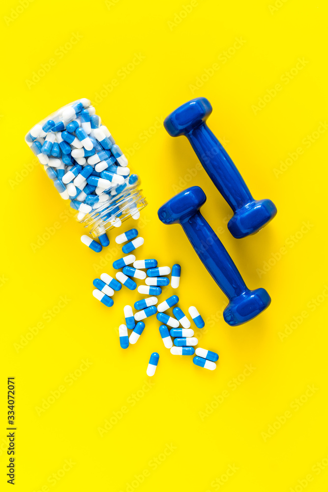 Dumbbells and creatine capsules - sport training concept - on yellow background top-down Dumbbells and creatine capsules - sport training concept - on yellow background top-down