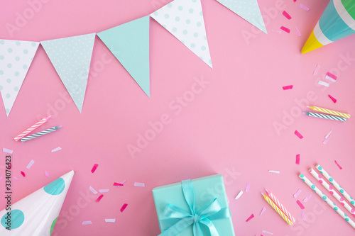 Birthday party background. Composition in pastel pink and mint colors. Birthday caps, gift box, party flags, drinking straws, confetti and candles. Top view, flat lay, copy space