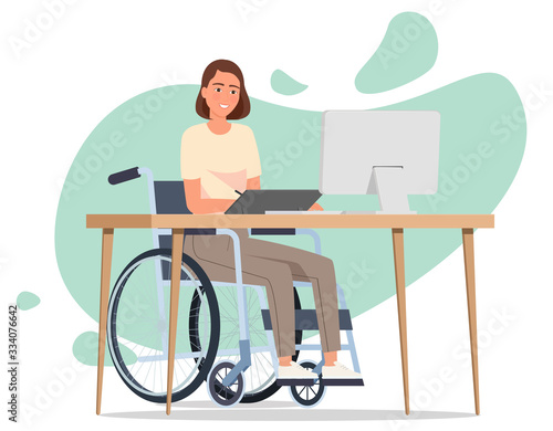 A girl in a wheelchair draws on a tablet at a table in front of a laptop.