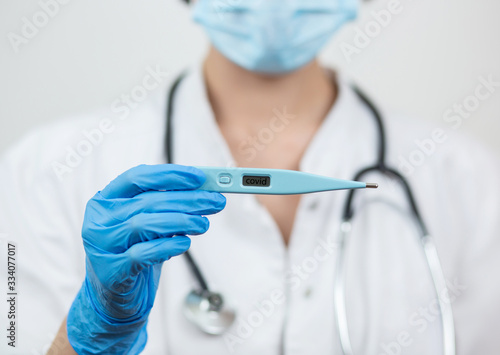 Close-up of a hand in a rubber latex medical blue glove holding an electronic thermometer in a mask. The concept of fever, malaise, fever, pain, coronavirus. Isolated on a white background.