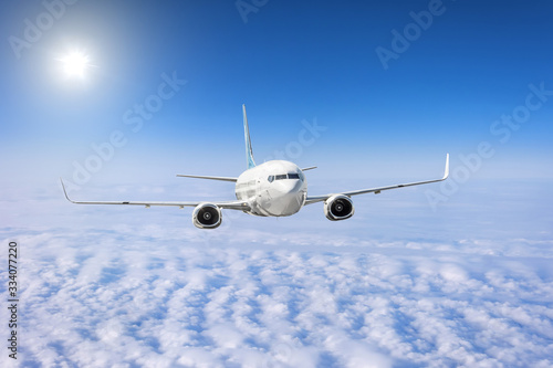 Passenger airplane flies in the sky over cloudscape and the bright sun shines.