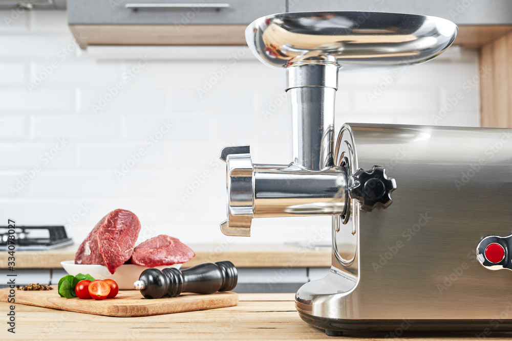 Meat grinder with fresh meat on a wooden table in kitchen interior