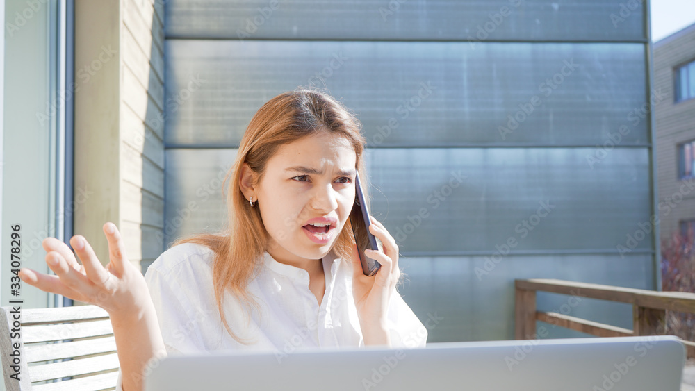 Angry businesswoman on phone behind computer working from home. Confused and unhappy female not understanding what is happening. Angry businesswoman on phone behind computer working from home. Confused and unhappy female not understanding what is happening.