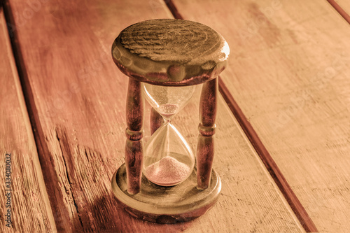 Time concept. A vintage hourglass with sand falling through, on a rustic background with a place for text, toned image © laplateresca