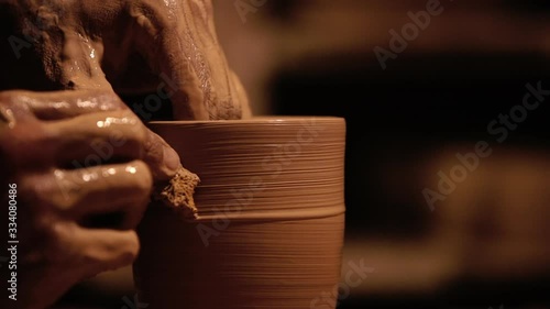 Young handsome sculptor shapes the clay product with pottery tools. Artisan potter prepares material for his pottery. Strong man hands working clay on potter's wheel. Work close-up.
