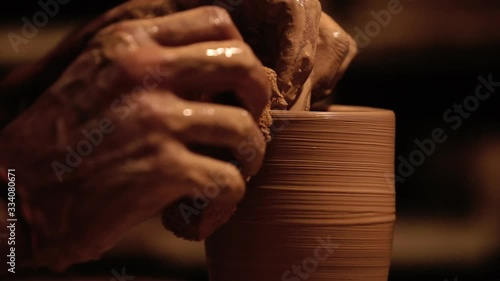 Young handsome sculptor shapes the clay product with pottery tools. Artisan potter prepares material for his pottery. Strong man hands working clay on potter's wheel. Work close-up. photo